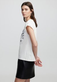 Witte katoenen t-shirt met opgerolde mouwen, voorzien van een zwarte bloemenprint aan de voorkant, gecombineerd met een zwarte leren minirok.