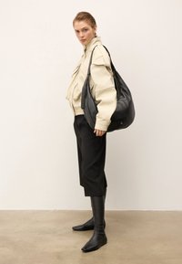 Kobieta w kremowej, strukturalnej kurtce, czarnych, krótko ściętych spodniach, wysokich, czarnych botkach do kolan i nosząca dużą, czarną skórzaną torbę na ramię.