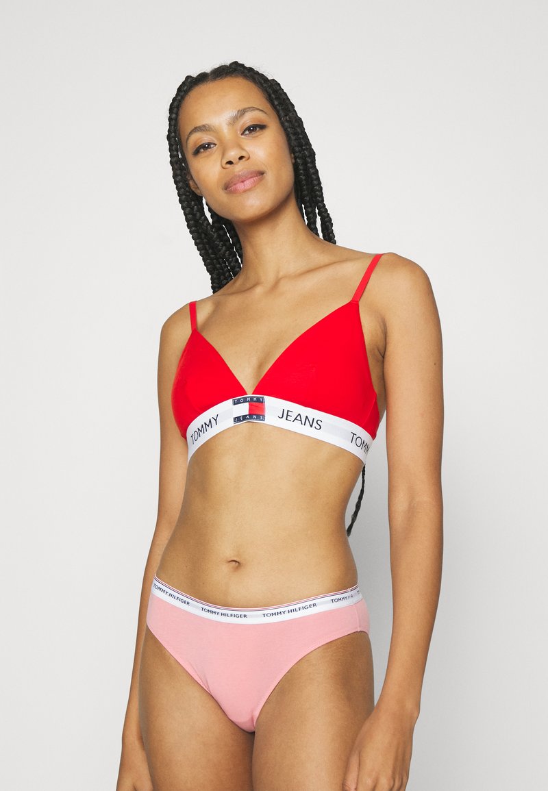 Bralette rouge avec une bande blanche arborant le logo "TOMMY JEANS", associée à un string rose avec une ceinture de taille assortie au logo.