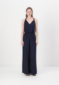 Navy Jumpsuit mit V-Ausschnitt und geknoteten Trägern. Hat einen gerafften Taillenbund und weite Hosenbeine, gefertigt aus einem glatten Stoff.