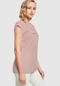 Lyserød t-shirt med korte ærmer, v-hals design og teksten "Pretty Woman" trykt i en mørkere nuance. Glat tekstur, afslappet pasform.