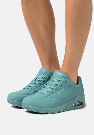 Light teal Skechers sneakers with perforated design, round toe, flat sole, and air cushioning. Features flat laces and stitched accents.