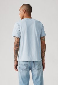 Lichtblauw T-shirt met korte mouwen en een relaxed fit, gemaakt van katoen. Heeft een nette halslijn en de drager heeft zichtbaar tattoo's op de armen.