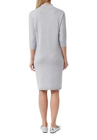 Graues Strickkleid mit Dreiviertelärmeln, taillierter Form und geripptem Kragen. Getragen mit metallisch silbernen Ballerinas.