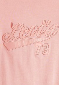 T-shirt rose clair avec logo "Levi's" en relief brodé et "73" dans une teinte légèrement plus foncée, au toucher lisse et au design décontracté.