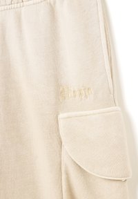 Jogger in cotone beige con tasca laterale e logo "Utopia" in rilievo. Tessuto testurizzato e design rilassato per il massimo comfort.