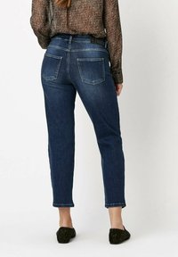 Jean en denim bleu foncé avec une coupe droite, dotés de deux poches arrière et de coutures contrastées. Portés avec des chaussures noires en texturé à enfiler.