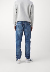 Mäns blå denimjeans med rak passform, har två bakfickor och en urtvättad stil. Matcher med en grå sweatshirt och vita sneakers.