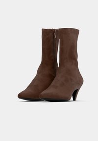 Καφέ μποτάκια από σουέντ με μυτερή μύτη και κωνικό τακούνι. Διαθέτουν διακριτικό φερμουάρ στο πίσω μέρος για κλείσιμο. Λείο υλικό.