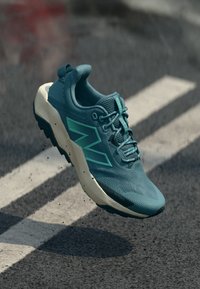 Türkisfarbener Sportschuh mit atmungsaktivem Mesh-Obermaterial, Schnürdesign und kontrastierender weißer Sohle. Verfügt über strukturierte Überzüge und ein Logo-Detail.