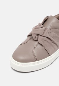 Baskets en cuir taupe avec semelle blanche, présentant un détail distinctif de nœud en tissu doux sur la partie supérieure avant.