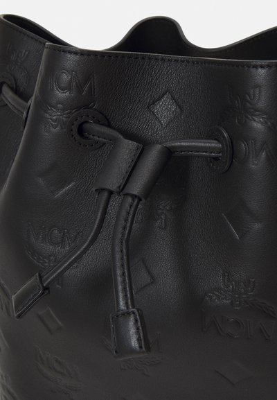 Borsa a secchiello in pelle nera con apertura a coulisse, marchio impresso e superficie texturizzata con finitura liscia. Accentuata da accessori coordinati.