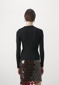 Svart ribbad långärmad topp med en figurnära design, kombinerad med en semi-transparent lagerkjol med dekorativa blomutfällningar och metallaccenter.