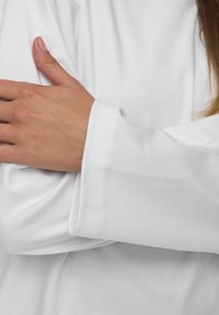 Biała koszula z długim rękawem o gładkiej fakturze, z szerokim mankietem i subtelnymi detalami szycia. Ręka spoczywa na tkaninie.