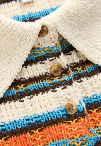 Zapínací svetr s krémovým límcem, zdobený vícebarevnými pruhovanými vzory v modré, hnědé, žluté a oranžové textuře. Viditelné čtyři knoflíky.