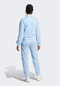 Fato de treino azul claro feito de um tecido macio, com gola alta e punhos elásticos, calças ajustadas e ténis brancos.