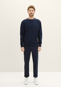 Granatowa bluza z okrągłym dekoltem i pasujące spodnie, wykonane z miękkiego materiału, w połączeniu z białymi trampkami. Prosty design i luźny krój.