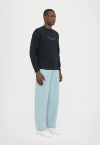 Zwarte sweatshirt met een ronde halslijn en lange mouwen, gecombineerd met lichtblauwe wijde jeans en witte sneakers. Eenvoudig logo detail.