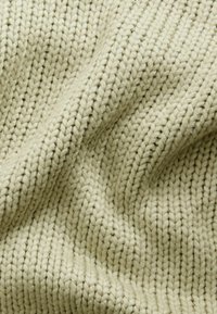 Pletená tkanina v světle béžové barvě s ribbed texturou a výraznými diagonálními stehy. Měkká, silná příze vytváří útulný vzhled.
