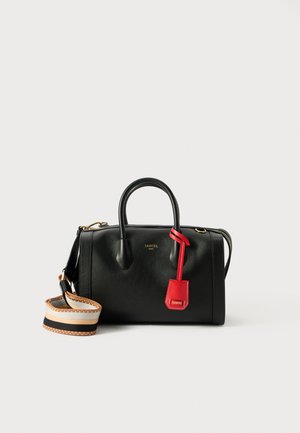 Sac à main en cuir noir avec double poignées, quincaillerie dorée, une étiquette rouge en accent et une bandoulière rayée amovible. Surface texturée lisse.