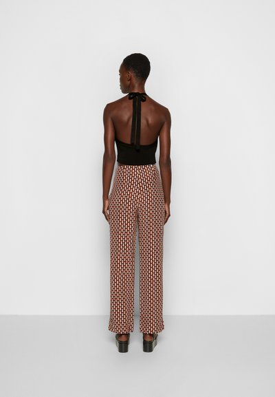 Top halter preto com costas abertas, combinado com calças largas de cintura alta com um padrão geométrico em marrom e creme. Sapatos de salto preto.