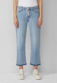 Helle blaue Jeans im geraden Schnitt mit umgeschlagenen Säumen und einem Kordelzugbund; kombinieren Sie sie mit weißen Sneakers für einen lässigen Look.