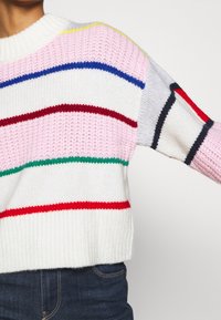 Pull tricoté avec un design raccourci, présentant des rayures horizontales en rose, rouge, bleu, vert et gris sur un fond blanc. Encolure côtelée.