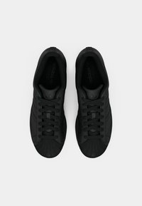 Une paire de baskets Adidas noires avec un design à embout en coque et des lacets, vue de dessus sur un fond blanc.