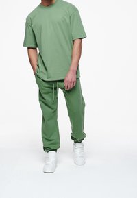 Zelené bavlněné tričko a odpovídající džínové kalhoty, volný střih, s kulatým výstřihem, stahovacími šňůrkami v pase a bílými teniskami. Hladký povrch.