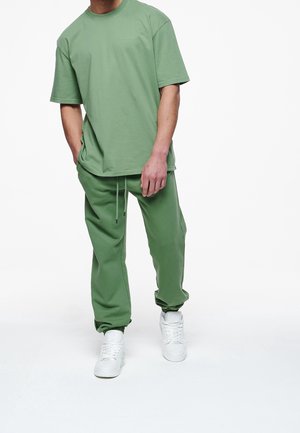 T-shirt en coton vert et joggings assortis, coupe décontractée, avec un col rond, une taille à cordon de serrage et des baskets blanches. Texture lisse.