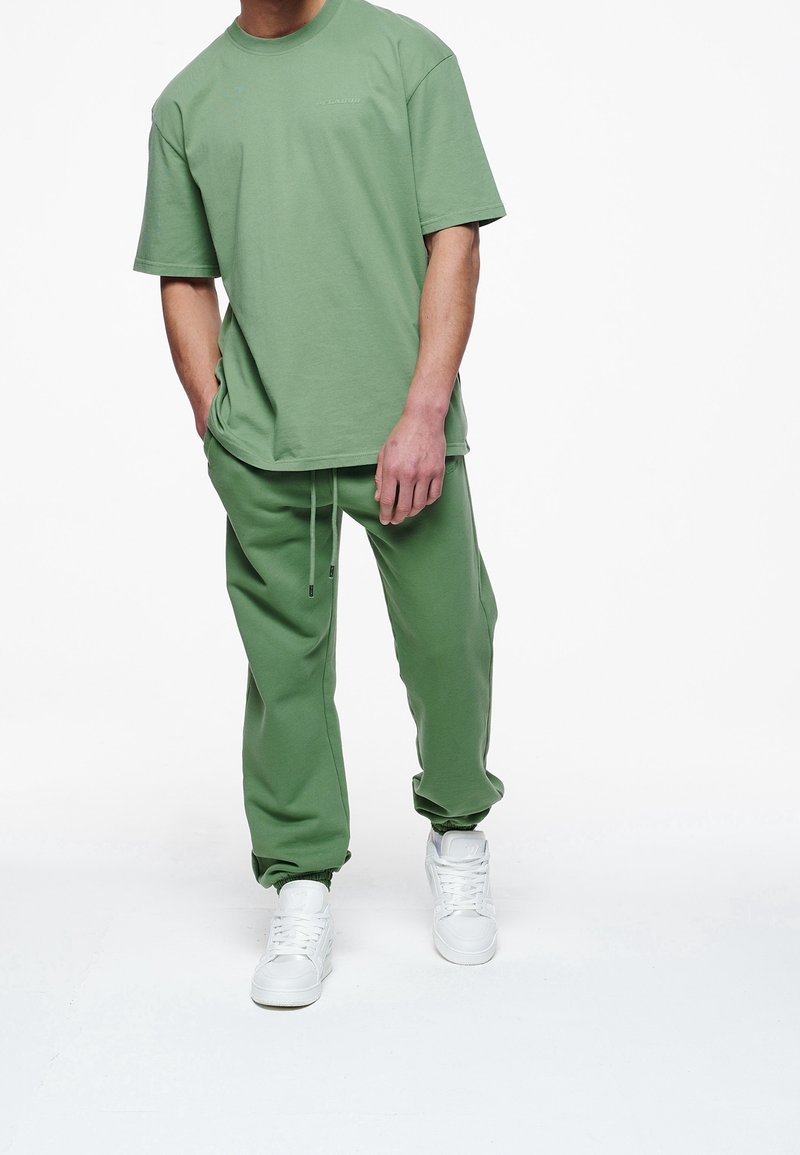 Zelené bavlněné tričko a odpovídající džínové kalhoty, volný střih, s kulatým výstřihem, stahovacími šňůrkami v pase a bílými teniskami. Hladký povrch.