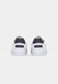 Vita sneakers med en slät läderfinish, med svarta accenter nära hälen och perforerade sidoventiler. Minimalistisk design, platt sula.