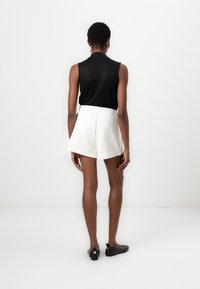 Black sleeveless top paired with white shorts featuring a tailored fit and pleated detailing, complemented by black flat shoes.