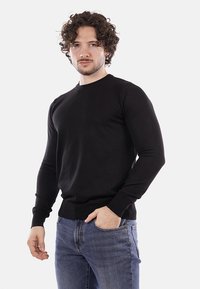 Maglione nero a collo tondo in cotone, con maniche lunghe e orlo a coste. Il modello è abbinato a jeans in denim lavaggio chiaro.