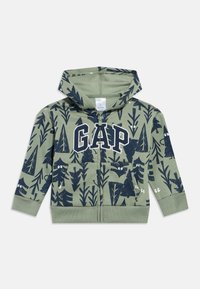Gyermek zöld cipzáras kapucnis pulóvere tengerészkék fák, állatok és szemek mintával, valamint nagy fehér GAP logóval a mellkason.