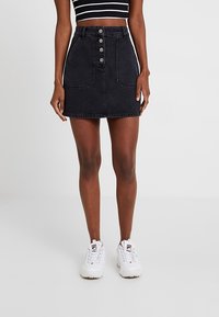 Jupe mini en denim foncé avec fermeture à boutons à l'avant, deux poches avant et une coupe ajustée, associée à des baskets blanches.