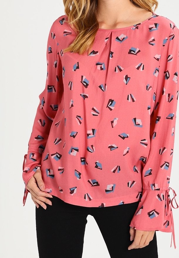 Rosa topp med abstrakta geometriska mönster i blått, svart och vitt. Långa ärmar med knytningar vid handlederna. Slätt, lätt tyg.