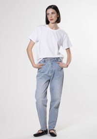 Camiseta de algodón blanca, jeans de tiro alto de color azul claro, ajuste relajado, con bolsillos laterales y detalles de costura. Zapatos planos negros complementan el conjunto.
