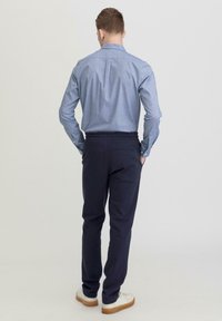 Lichtblauwe overhemden met een rugplooidetail; marineblauwe broek met een elastische tailleband en achterzak; gecombineerd met witte sneakers.