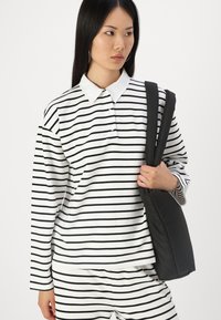 Striped long-sleeve polo shirt in white and black with a buttoned collar, paired with matching striped pants. Black shoulder bag with padded straps.
