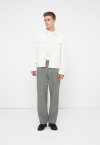 Fehér farmerdzseki, két mellzsebbel, világos színű ing felett viselve, szürke kockás nadrággal. Fekete cipők egészítik ki az öltözetet.