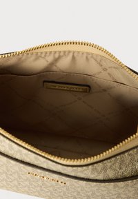 Sacca in tessuto dorato con chiusura a zip. L'interno presenta una fodera beige con un motivo a logo del marchio ripetuto e un'etichetta del marchio.