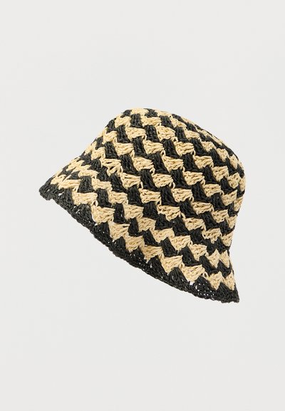 Πλεκτό καπέλο τύπου κάδου με μοτίβο εναλλασσόμενων μαύρων και φυσικού χρώματος ινών, με χαλαρή γείσο και υφή φινιρίσματος.