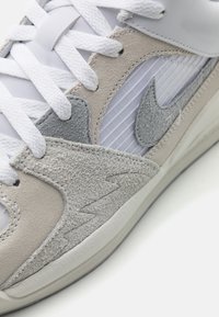Gros plan d'une chaussure de sport grise et blanche montrant des panneaux en daim texturé, des lacets blancs et le logo Nike swoosh cousu sur le côté.