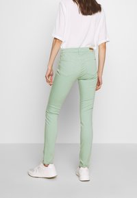 Jeans skinny de color verde menta, hechos de una suave mezcla de algodón, con bolsillos traseros y una etiqueta de cuero en la cintura. Combinados con zapatillas blancas.
