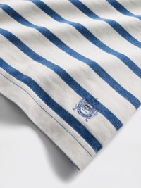 Bomullsstoff med horisontale blå og hvite striper. Har en blå brodert logo på den ene kanten, med en glatt og myk tekstur.