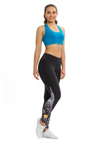 Black leggings with a patterned side panel featuring a floral design, paired with a bright blue sports bra and white sneakers.