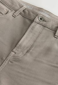 Beige kitsas lõikega püksid, mis on valmistatud siledast puuvillasegusest kangast. Omab eespool taskuid ja metallist nööbi sulgurit. Õmblusdetailid kogu ulatuses.