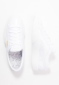 Weiße Sneakers mit glänzender Lederoberfläche, runder Spitze, strukturiertem Profil und subtilem goldenen Logo. Mit weißen Schnürsenkeln und gemustertem Innenfutter.