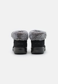 Stivali alla caviglia in suede neri con risvolto in pelliccia sintetica grigia, suole in gomma e cerniere laterali per una facile calzata, caratterizzati da un design minimale e una forma ergonomica.